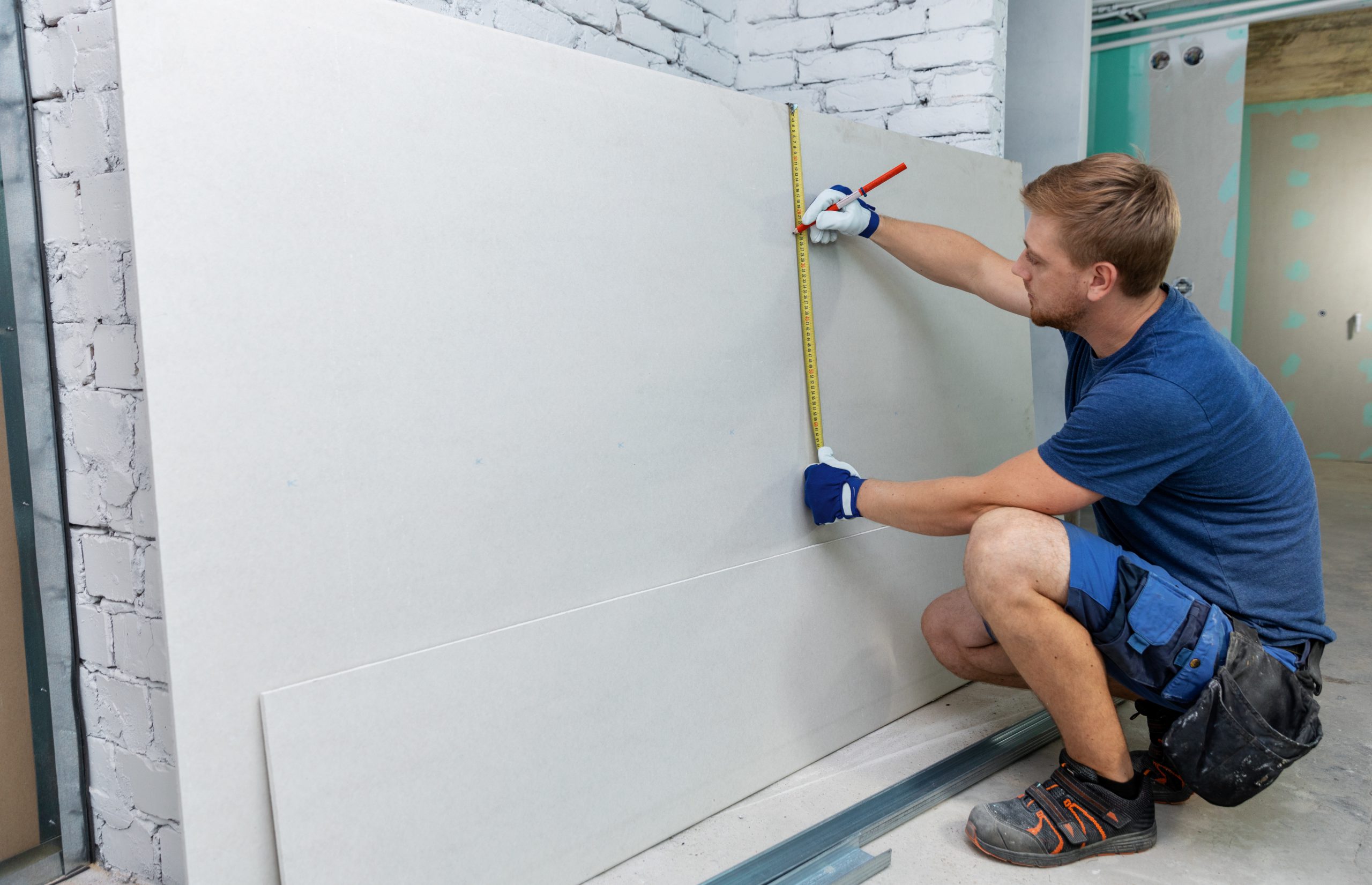 man measuring plasterboard sheet for interior construction